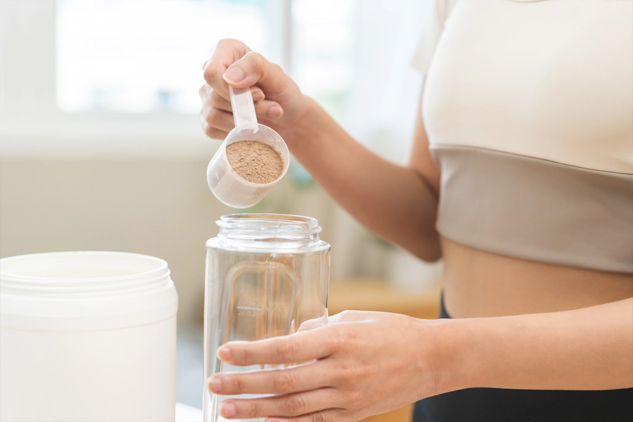 woman in sportswear, hand in holding scoop adding protein powder into bottle